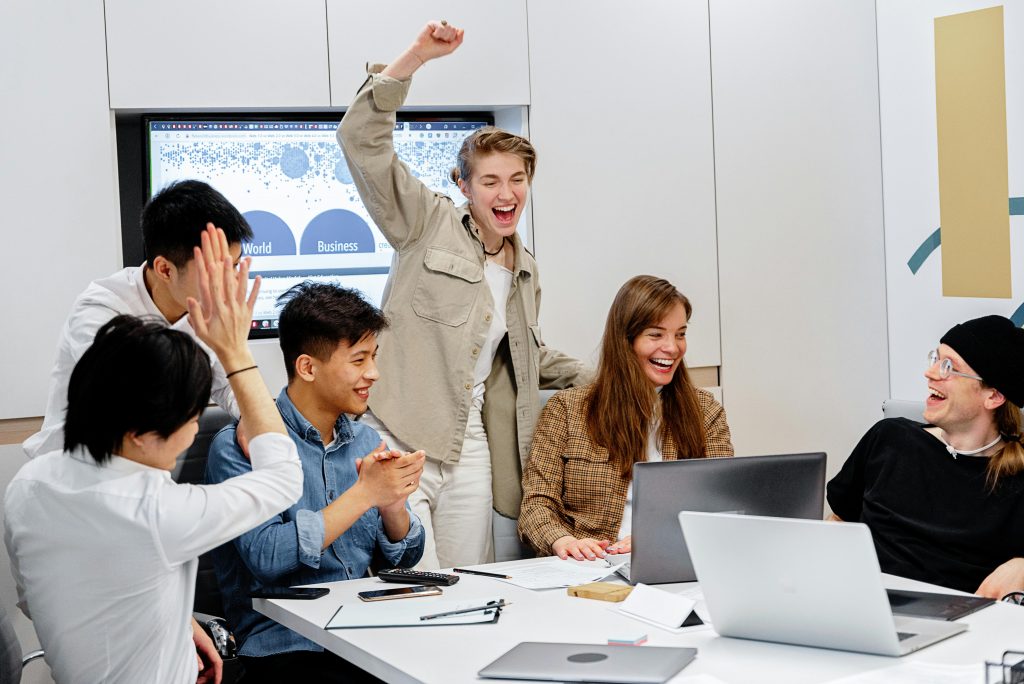 pexels-photo-7988237-7988237 A diverse team enthusiastically celebrating success around laptops during an office meeting.